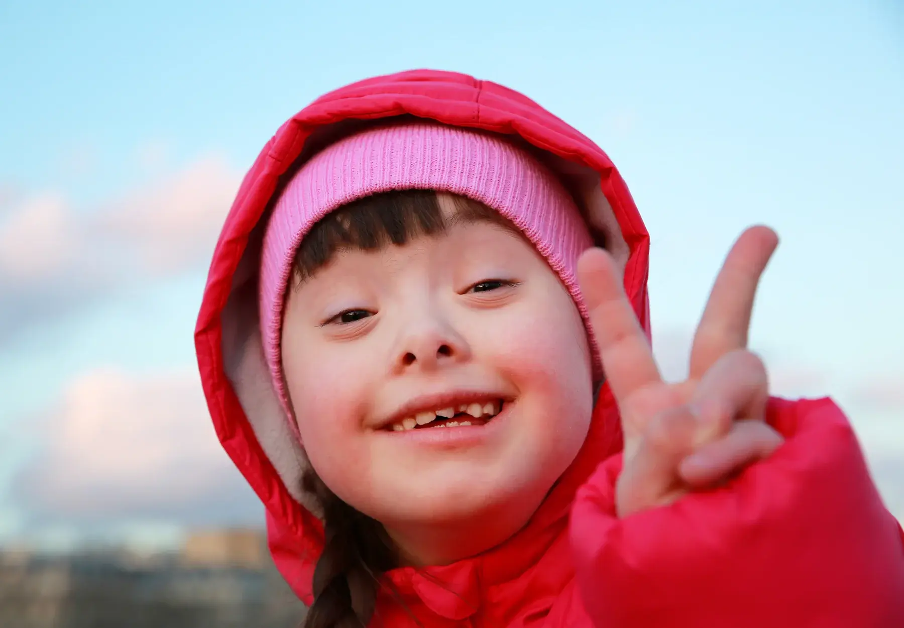 A smiling child making a peace sign outdoors